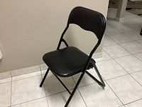 Single black folding chair from the side showing metal frame and padded seat and backrest in faux leather.