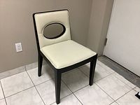 Full view of a cream faux leather dining chair with black legs, showing overall design and shape.