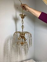 Chandelier held up showing gold metal frame with hanging crystal rods and beads