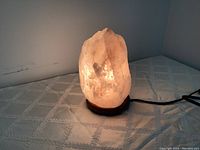 Himalayan salt lamp turned on, showing warm orange-pink glow, wooden base and electrical cord visible.