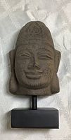 Happy Buddha sculpture face and base stand visible with neutral fabric background.
