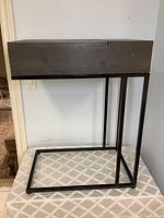 Side view of the wooden side table showing metal open rectangular frame base and scratched dark wooden top with compartment.
