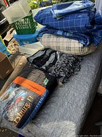 Photo showing stacked comforters and the throw blanket on an outdoor surface with plastic storage bins nearby.