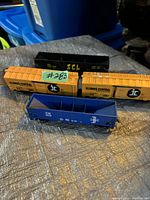 Four vintage HO scale model train cars on a textured surface with blue storage bins in background