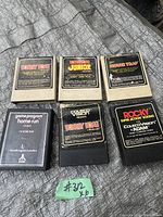 Photo showing six vintage video game cartridges including four Atari 2600 titles and two ColecoVision cartridges, placed on a fabric surface with a green slip labeled '#312'.