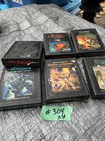 Photo of six vintage Atari game cartridges arranged on a surface, showing front labels of each game