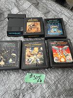 Six Atari 2600 game cartridges placed on a textured surface, labels facing the camera. Includes Astroblast, Warlords, Video Pinball, Asteroids, Missile Command, and Yars Revenge titles. The cartridges show normal age wear.