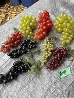 Photo of nine vintage decorative plastic grape clusters in various colors arranged on a brown surface outdoors. Colors include red, yellow-green, black, maroon, and light green.