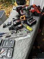 Photo showing the assortment of power tools on a tarp outside including cordless drills, Black & Decker hand planer, Ryobi oscillating tool, circular saw, battery packs, chargers, drill bits and accessories.