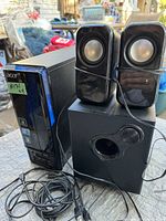 Acer desktop tower, subwoofer, and two satellite speakers on outdoor table with background clutter.