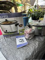 Bravetti slow cooker box, slow cooker unit, mini cooker, and instruction manual on a grey surface outdoors.