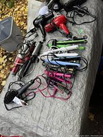 Photo shows assorted hair care appliances laid out on a grey cloth surface outdoors. Includes multiple hair dryers, hair straighteners, and curling irons with cords visible.