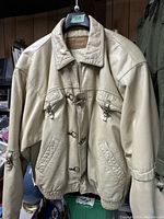 Front view of men's vintage beige leather jacket showing toggle front closure, zippered pockets, collar, and visible stain on one sleeve.