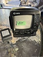 Front view of the Curtis portable TV showing screen, control knobs, AM/FM radio dial, and power adapter placed beside it.