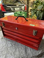 Closed vintage red metal toolbox with handle and locks showing age wear