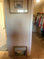 Two framed artworks displayed on a wall and floor: a black and white bird print and a color landscape painting.