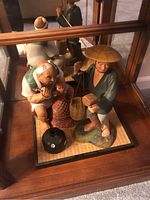 Two Asian statues on a mat inside a display case, showing both figures and a small black round pot.