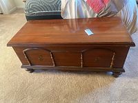 Front view of the cedar lined blanket box showing the reddish-brown wood, decorative front panels with spindle details, and bun feet.