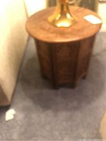 Full view of one round-top carved wooden octagonal side table on blue carpet near sofa. Slightly blurred.