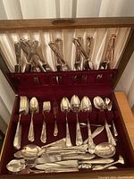 Full open wooden box showing the flatware set, including knives, forks, spoons, salad forks, and serving utensils placed in designated slots with velvet lining.