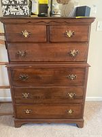 Front view of wood tall boy dresser showing four drawers with brass handles, visible scratches on wood surface.