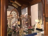 Wide view of five tall painted floral wine glasses with carved ivory figurine and decorative eggs reflected in the cabinet mirror.