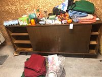 Photo showing wooden cabinet, assorted tablecloths in red and green colors, decorative ornaments including seasonal pumpkins, and various household items.