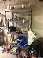Five-level metal shelving unit with various hardware and cleaning supplies, extension cord, and storage items placed in a basement setting.