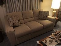Front view of full sofa with both throw pillows on carpeted floor under lamp