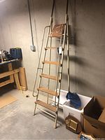 Full ladder upright showing metal frame, six wooden steps, and a wooden platform at the top with paint stains.