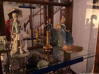 Display cabinet with figurines and decorative pieces including Lladro girl figurine, gold leaf dish, Franklin Mint woman figurine, vase, salt and pepper shakers.