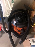 Ridgid orange and black shop vacuum with attached black hose coiled around it.