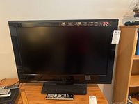 Front view of Toshiba 32-inch TV with screen off, shows model and size sticker on top right corner, sits on wooden furniture.