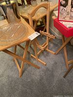 Four wooden TV trays with crossed folding legs with a wooden stand to hold them shown in a corner with other items.