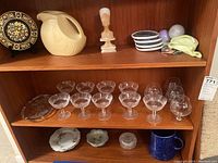Shelf displaying 9 clear Waterford crystal glasses of various stemmed types, some small plates and stoneware mug below.
