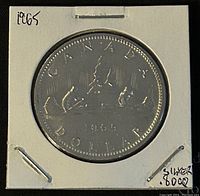 Photo of the reverse side of the 1965 Canadian silver one dollar coin showing the canoe and figures with date and inscriptions.