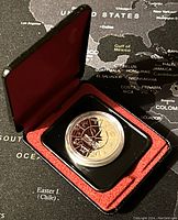 Photo of the Canadian silver dollar coin displayed in an open hinged black case with red lining, highlighting the coin's face design.