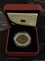 Coin inside red presentation box with certificate booklet under lid.