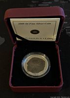 Coin displayed in red cushioned case with informational card behind it, showing presentation and storage condition