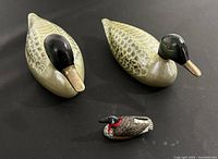 Photo of two medium-sized ceramic duck figurines and one small wooden duck figurine on black surface.
