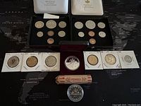 Two black cases containing 1971 and 1977 Canadian uncirculated coin sets with eight coins each and assorted loose coins including a penny roll in front.