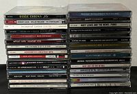 Stack of rock music CDs side view showing titles and artists over 30 assorted cases.
