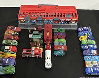 Wide overhead view of the 40+ Disney Cars die cast cars, trucks, and a red pit stop stand arranged on a black surface.