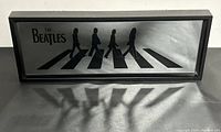 Front view of The Beatles Abbey Road silhouette framed mirror, showing the band members crossing the street in black on a mirrored background.