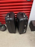 Side view showing two black hard shell luggage cases with top handles and zip closures.