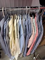 Full view of all 11 assorted men's button-up dress shirts on hangers showing variety of colors and patterns including striped, checkered and solid shirts.