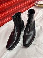 Pair of black leather men's ankle boots, square toe, side zipper closure, smooth leather upper, rubber sole.