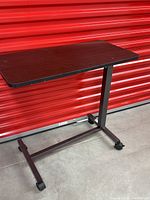 Side view of the adjustable height over bed table showing metal frame, casters, and tabletop surface.
