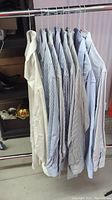 Eight men's dress shirts hanging on hangers, assorted striped colors including beige, blue, and white tones.