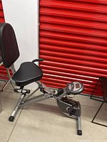 Side view of adjustable silver metal recumbent fitness bike showing padded seat, backrest, and pedal with electronic display.